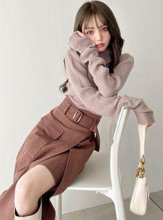 Woman with long brown hair wearing a turtleneck and midi skirt, sitting on a chair