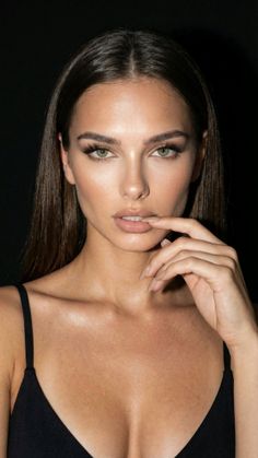 Woman with long dark hair and green eyes in a black top, biting her finger