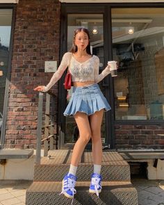 Woman in a denim skirt and crop top posing outdoors with a coffee cup