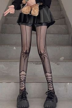 Person in fishnet stockings with spider web pattern and a black skirt holding a teddy bear