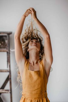 Woman with curly blonde hair in a yellow dress, arms raised, looking up