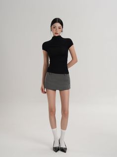 Woman in a black top and grey mini skirt posing in a studio