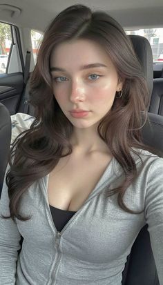 Woman with long brown hair and blue eyes wearing a grey hoodie in a car