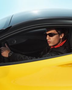 Man in sunglasses and a black jacket driving a yellow car