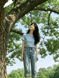 Woman in a blue t-shirt and jeans standing under a tree, looking up and smiling