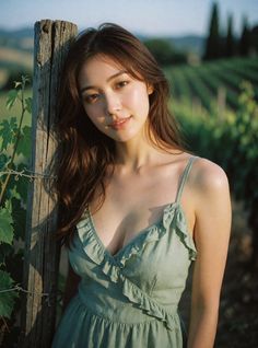 Woman in a green dress leaning on a wooden post in a vineyard