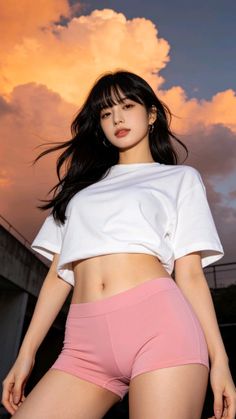 Woman with long black hair in a white crop top and pink shorts at sunset