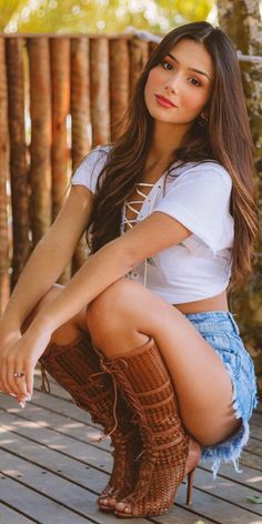 Woman in denim shorts and a lace-up top squatting outdoors