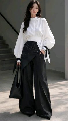 Woman in a white blouse and black wide-leg pants holding a black bag outdoors