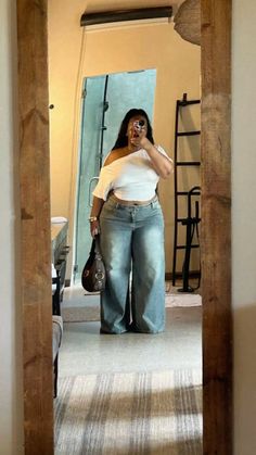 Woman in a white off-shoulder top and wide-leg jeans taking a mirror selfie