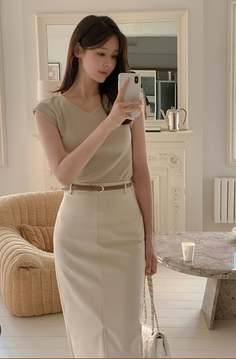 Woman in a neutral-colored top and midi skirt taking a mirror selfie indoors