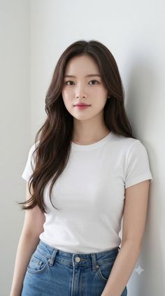 Woman with long brown hair wearing a white t-shirt and blue jeans, leaning against a wall
