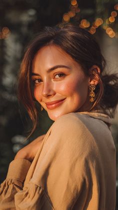 Woman with brown hair and earrings smiling in soft golden hour light