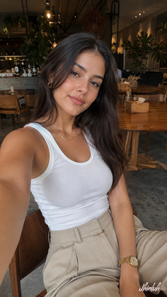 Woman with long dark hair wearing a white tank top and khaki pants in a cafe