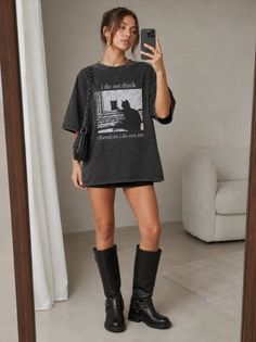 Woman in an oversized t-shirt and black boots taking a mirror selfie