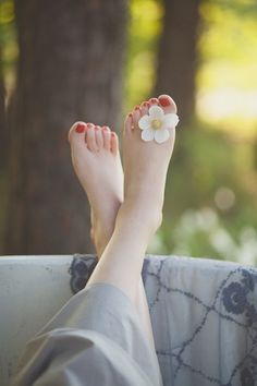 Feet with red nail polish and a white flower, crossed and resting outdoors
