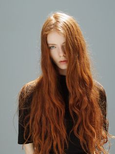 Person with long red hair and blue eyes wearing a black shirt in a studio setting