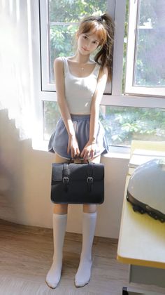 Woman in a white tank top and blue shorts holding a satchel by a window