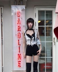 Woman with black hair wearing a crop top and shorts standing next to a neon sign