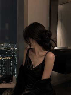 Woman in a black dress looking out at a city night view