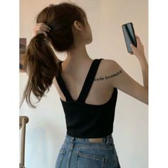 Woman with long hair in a ponytail, wearing a black top and denim jeans, holding a phone