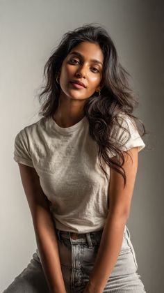 Woman with long dark hair wearing a white t-shirt and jeans, looking at the camera