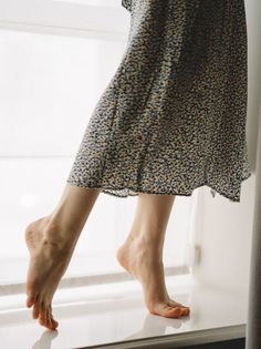Woman in a floral dress standing on tiptoes with bare feet indoors