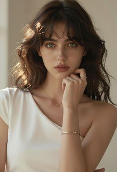 Woman with green eyes and wavy brown hair wearing a white top and jewelry