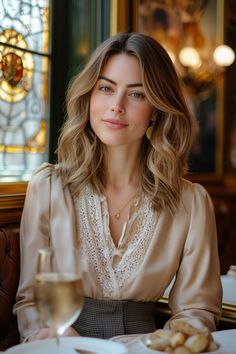 Woman with wavy blonde hair wearing a lace-trimmed blouse in a restaurant