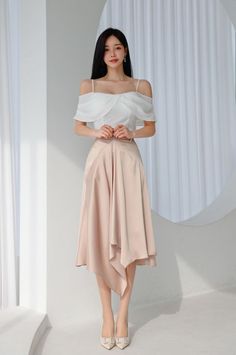 Woman in a white off-shoulder top and a pink asymmetrical skirt standing indoors