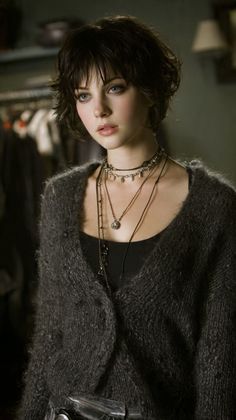 Woman with short dark hair wearing a cardigan and multiple necklaces indoors
