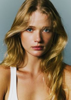 Woman with blonde hair and blue eyes wearing a white tank top