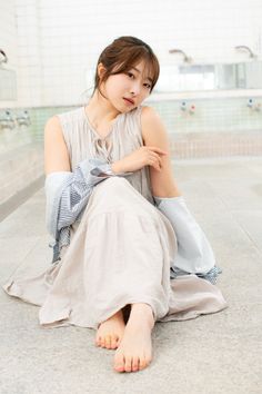 Woman in a long light-colored dress sitting barefoot indoors