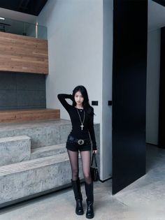 Woman in a black long-sleeve shirt and shorts with black boots indoors