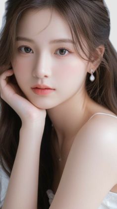 Woman with long brown hair and pearl earrings, resting her chin on her hand