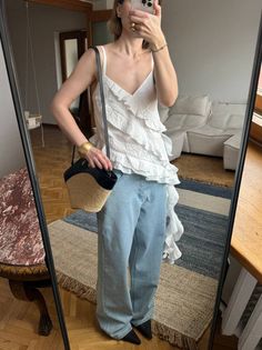 Woman in a white ruffled top and wide leg jeans taking a mirror selfie