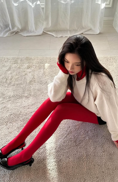 Woman in red tights and a white sweater sitting on a rug indoors