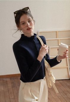 Woman in a navy cardigan holding a coffee cup and a tote bag indoors