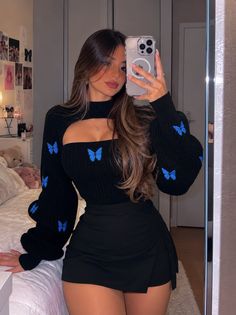 Woman in a black top with butterfly print and a black skirt taking a mirror selfie