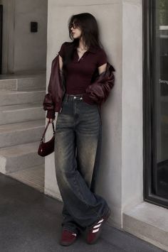 Woman in a maroon top and wide leg jeans leaning against a wall outdoors