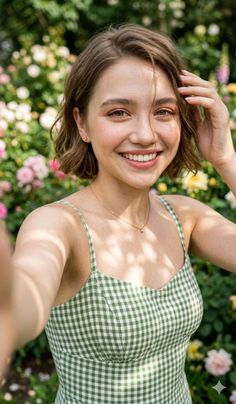 Smiling woman with short hair in a green gingham dress taking a selfie in a garden