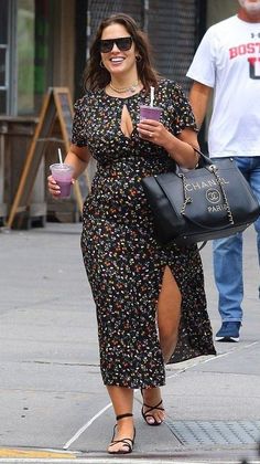 Woman in a floral dress and sunglasses walking on a street with drinks