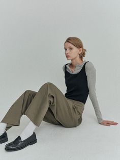 Woman with blonde hair in a bun, wearing a long sleeve shirt and wide leg pants, sitting on the floor