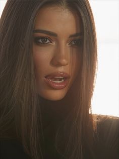 Woman with long dark hair and glossy lips in a backlit portrait