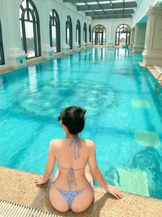 Woman in a blue bikini sitting at the edge of an indoor swimming pool
