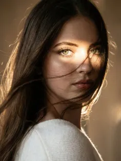 Woman with long hair and green eyes in a white sweater with dramatic backlight