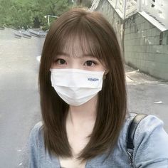 Woman with brown hair and bangs wearing a white mask and gray cardigan outdoors