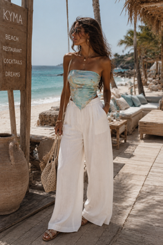 Woman in a bandana top and wide leg pants on a beach boardwalk