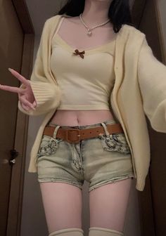 Person in a crop top, cardigan, and denim shorts showing peace sign