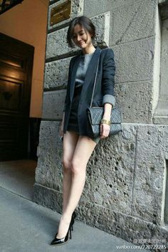 Woman in a blazer and mini skirt leaning against a stone wall